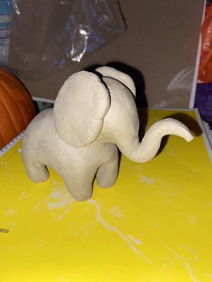 an elephant figurine sitting on top of a yellow surface next to pumpkins