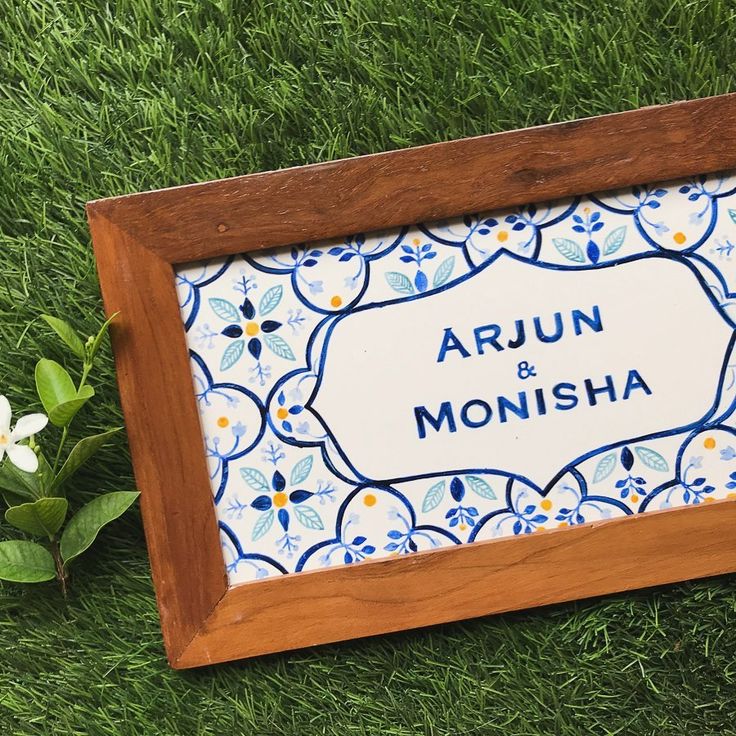 a wooden frame sitting on top of green grass next to white and blue flowers with the words arjun & moisha written in it