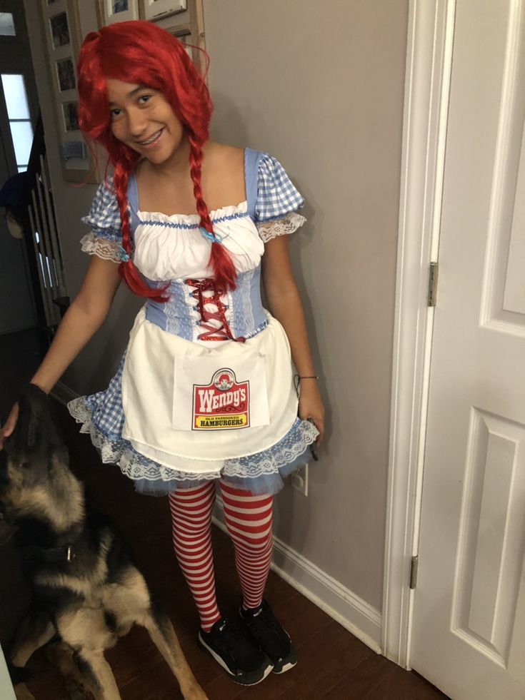 a woman with red hair is standing next to a dog and wearing a white apron