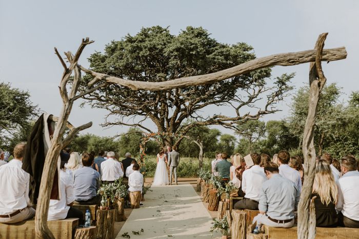 a group of people that are standing in front of some trees and chairs at a wedding