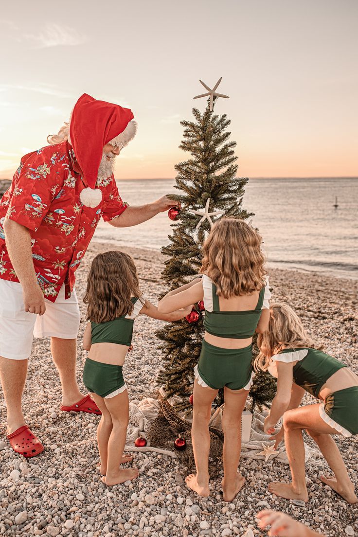 a group of young children standing around a christmas tree on the beach with an adult