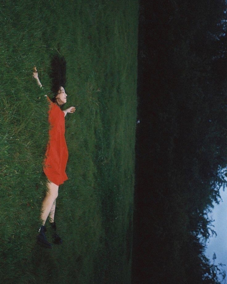 a woman in a red dress is throwing a frisbee on the grass outside