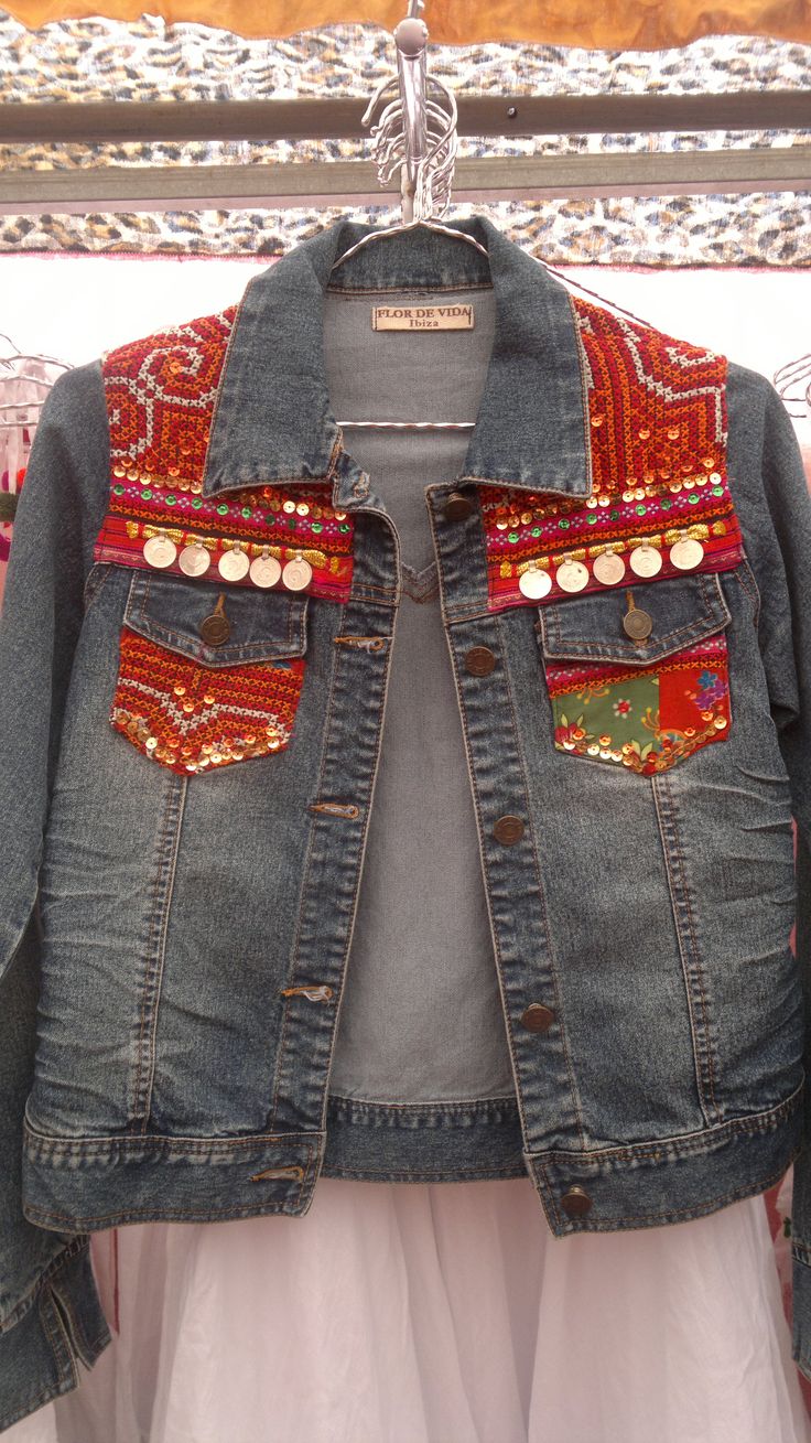 a denim jacket with colorful patches and buttons on the back, hanging from a clothes rack