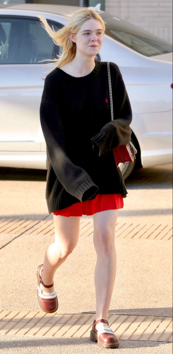 a woman in black sweater and red shorts walking down the street with her hand on her hip