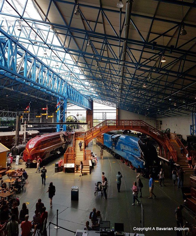 people are walking around an indoor museum with two trains on display and one train is red