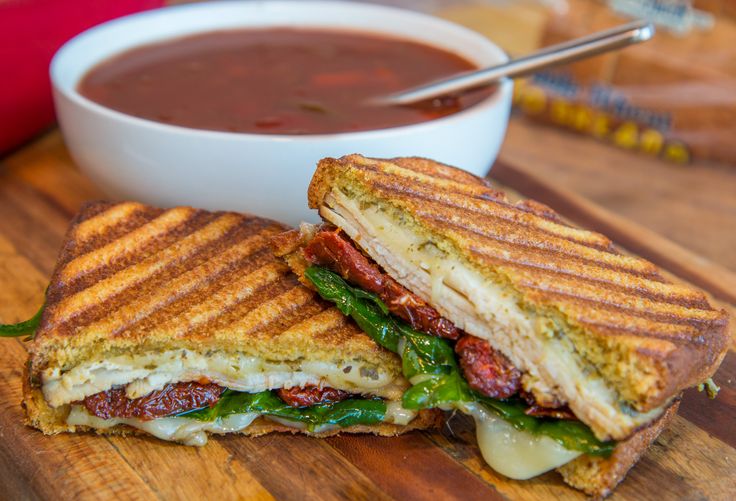 a grilled sandwich on a cutting board next to a bowl of soup