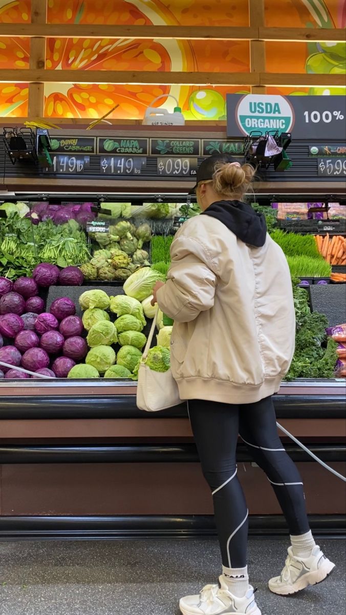 a woman standing in front of a produce section at a grocery store with her back to the camera