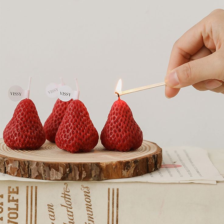 three strawberries on a wooden stand with a match between one candle and the other