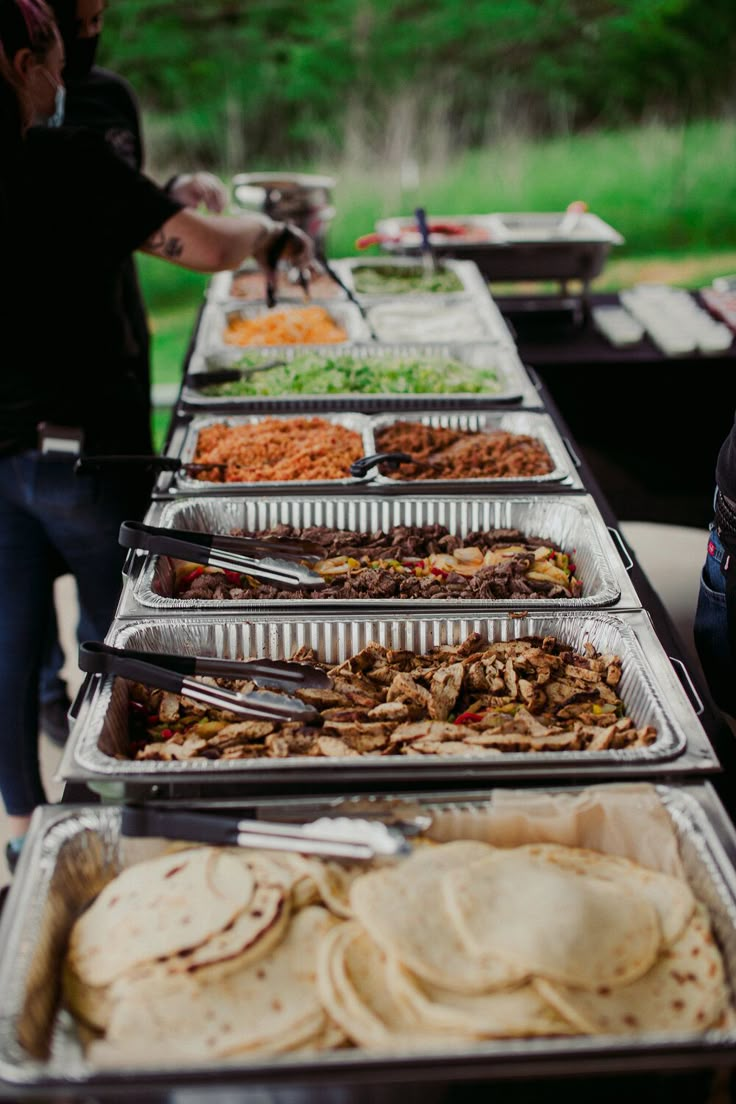 several trays of food are lined up on a table with people in the background