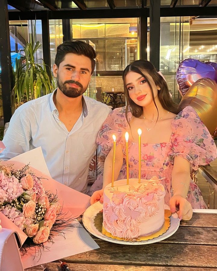 a man and woman sitting at a table with a cake in front of them that has candles on it