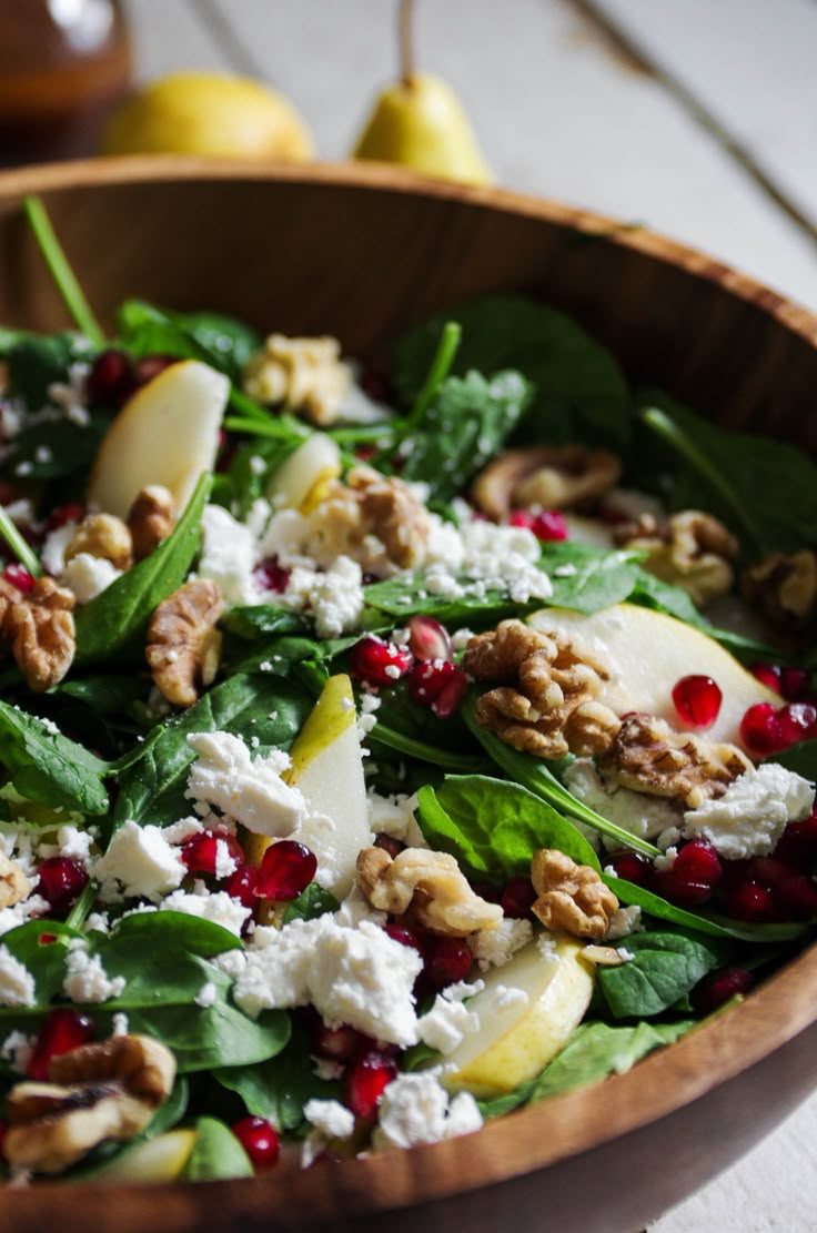 a wooden bowl filled with spinach, pears and feta cheese topped with walnuts