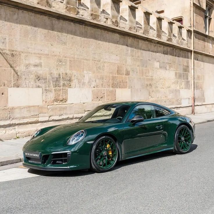 a green sports car parked in front of a stone building on the side of a street