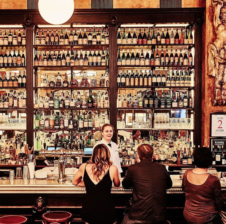 people are standing at the bar in front of shelves full of liquors and bottles