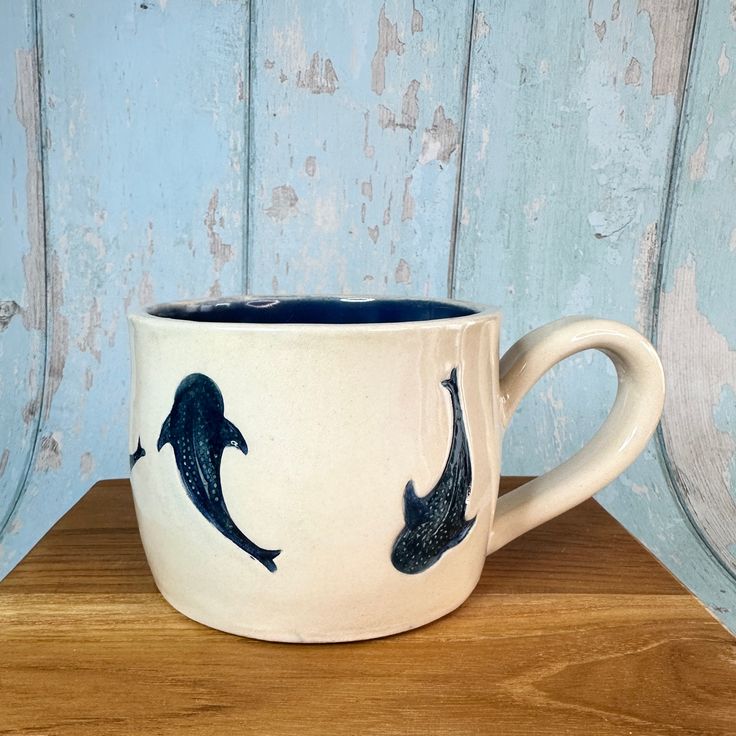 a coffee cup with two dolphins painted on the outside and inside, sitting on a wooden table