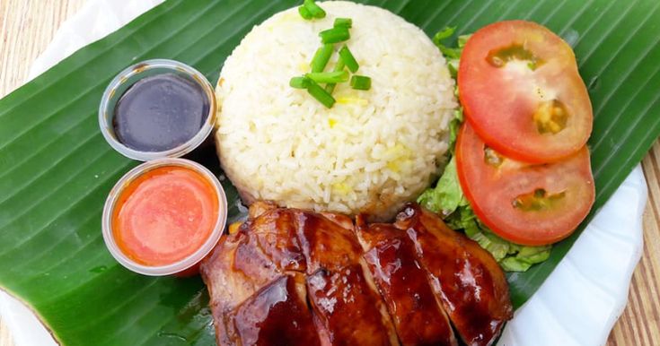 a plate topped with meat and rice next to sauces on a leafy green surface