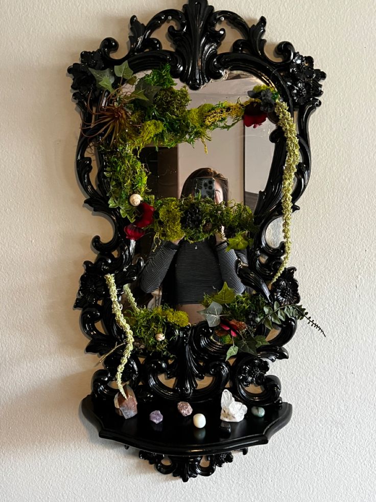 a mirror that is hanging on the wall next to a shelf with plants and rocks