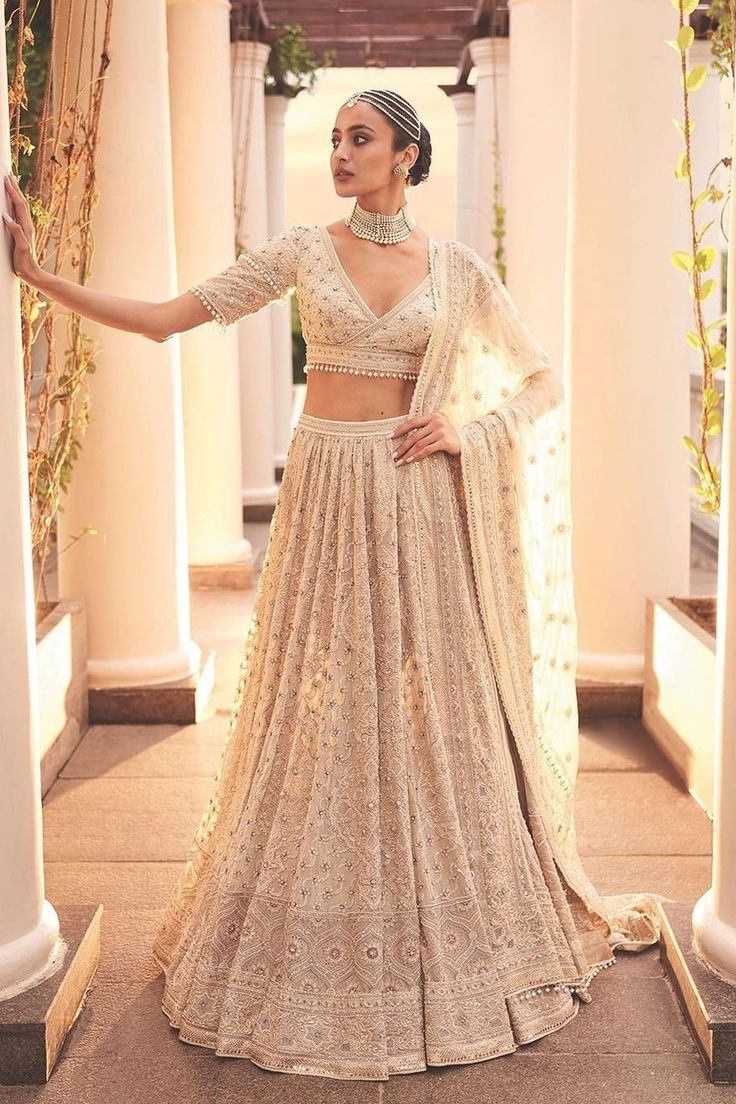 a woman in a white and gold lehenga standing on a walkway with her arms outstretched