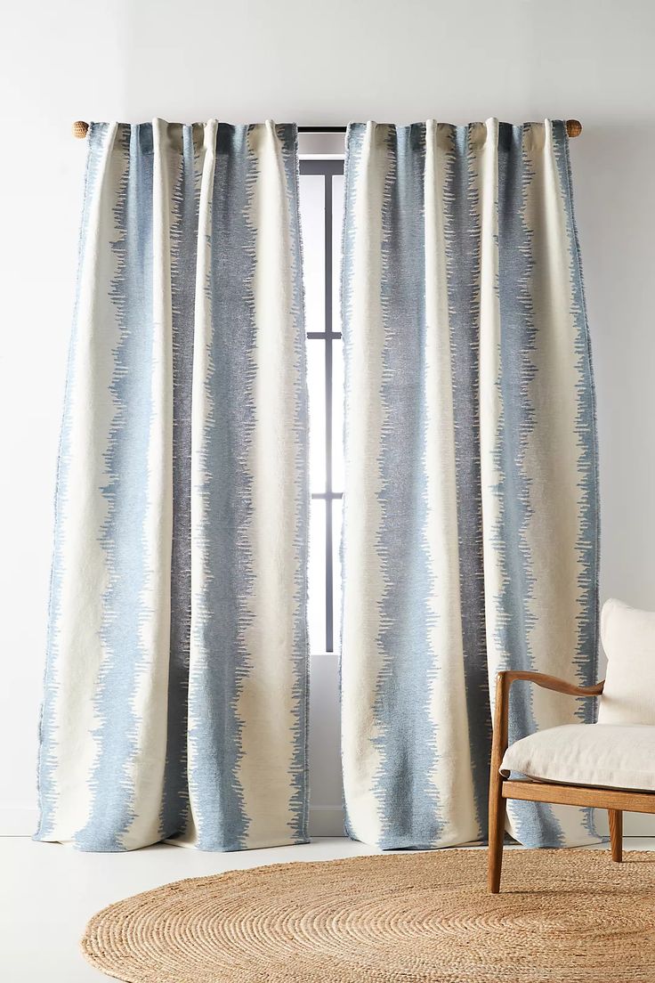 a chair sitting in front of a window with blue and white drapes on it