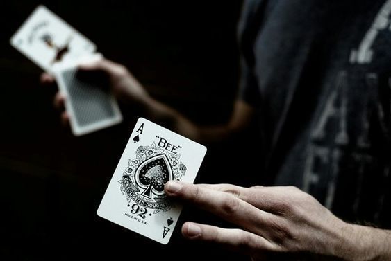 a man holding two playing cards in one hand and an ace in the other with both hands