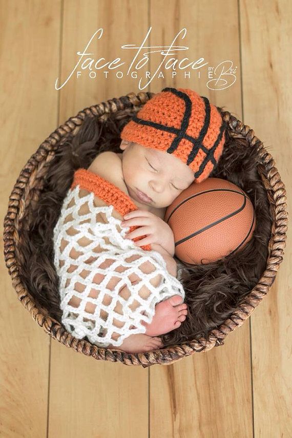 a baby in a basket with a basketball on it's head and wearing an orange knitted hat