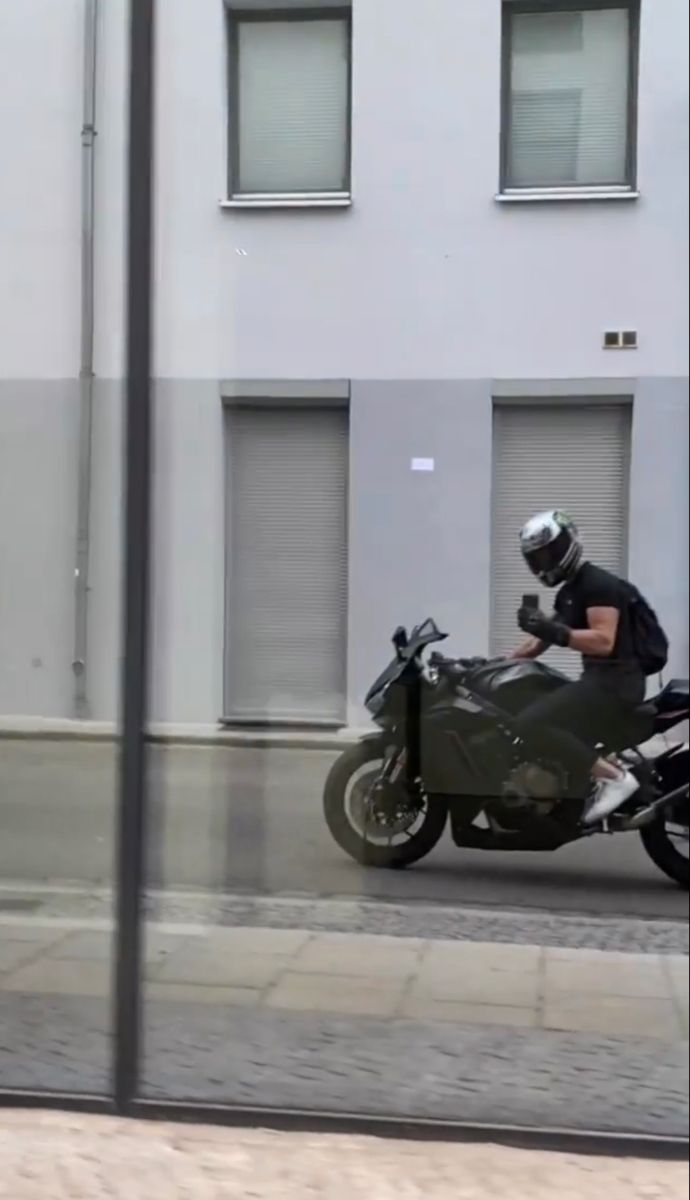 a man riding on the back of a motorcycle next to a tall white building with windows