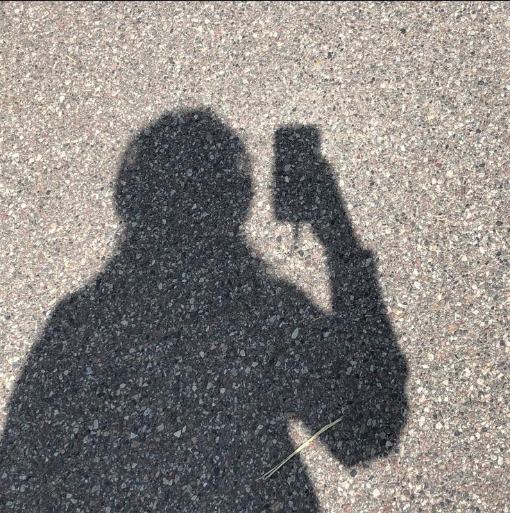 the shadow of a person holding a cell phone up to their face, on asphalt