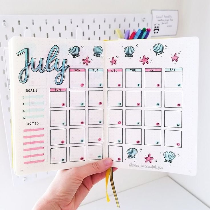 a hand holding up a planner with the word july on it and seashells