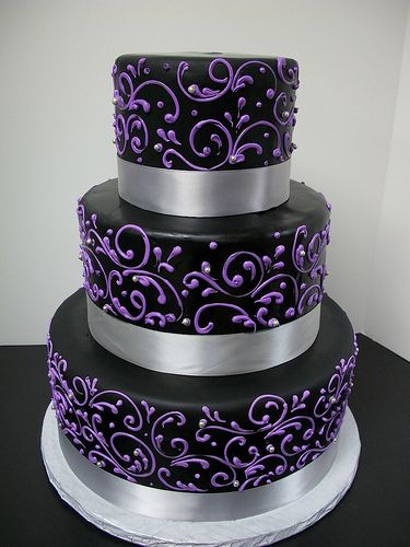 a three tiered cake with purple and silver decorations on the top, sitting on a black table