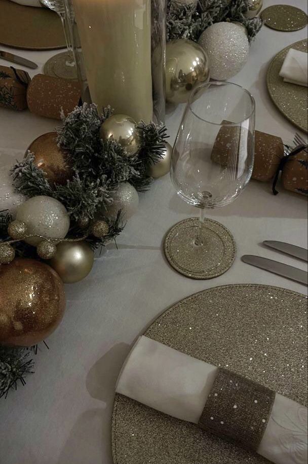 the table is set for christmas dinner with silver and gold decorations, candles, and plates