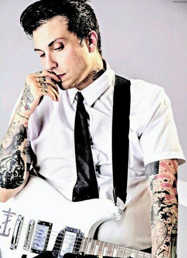 a man with tattoos holding an electric guitar in his right hand and looking at the camera