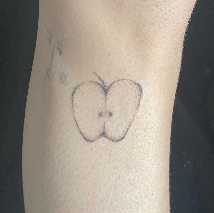 an apple tattoo on the leg of a person's left arm, with two apples in the middle