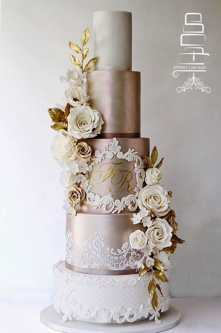 a three tiered wedding cake with white flowers and gold leaves on the top layer