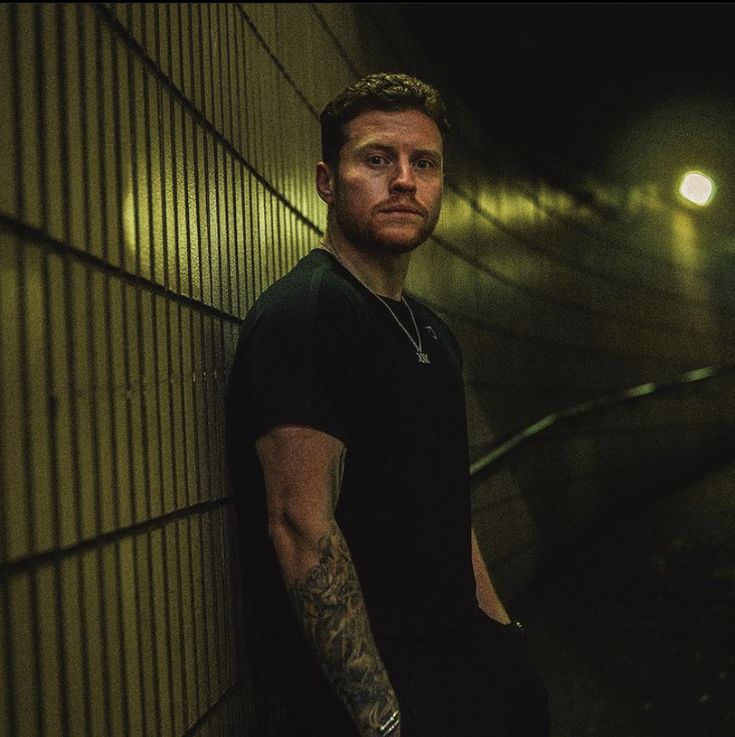 a man with tattoos leaning against a wall