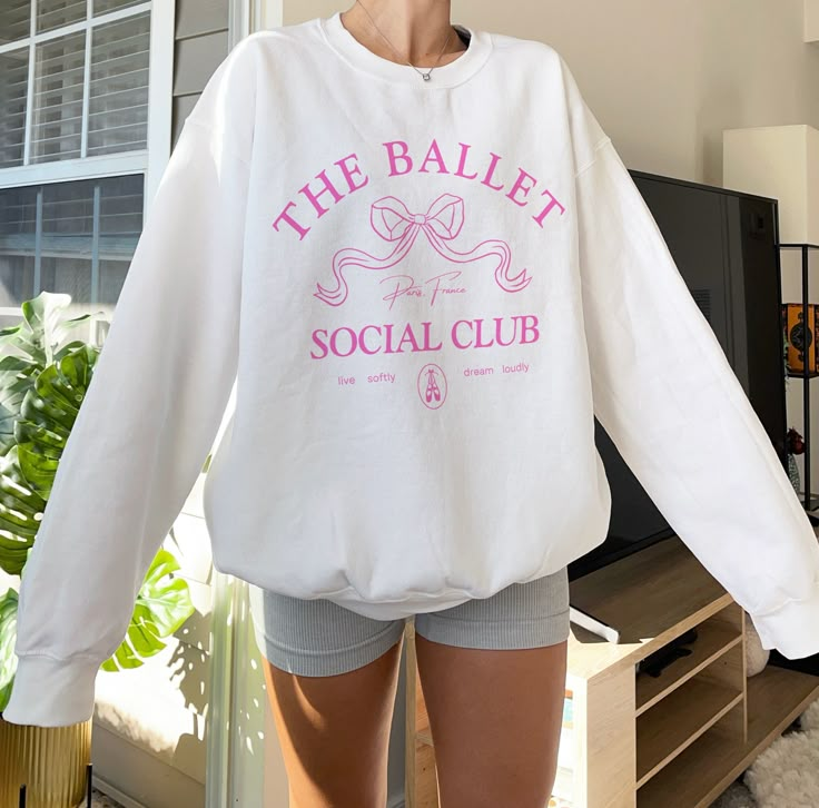 a woman is standing in front of a television wearing a sweatshirt that says the ballet social club