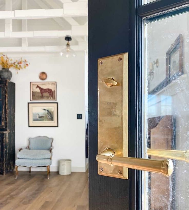 a door handle on a black door in a room with wooden floors and white walls