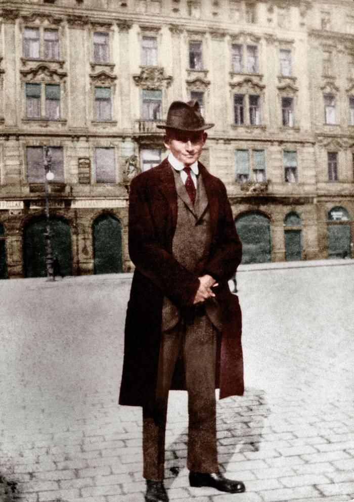 an old photo of a man standing in front of a building wearing a hat and coat