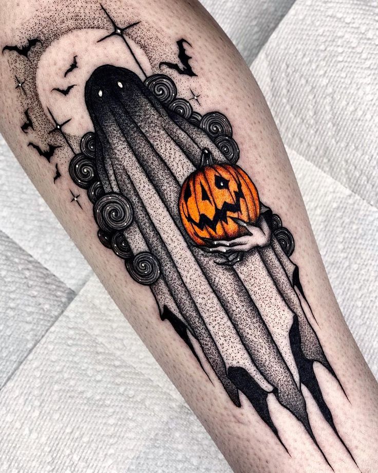 a halloween themed tattoo on the leg of a person with an orange jack - o - lantern