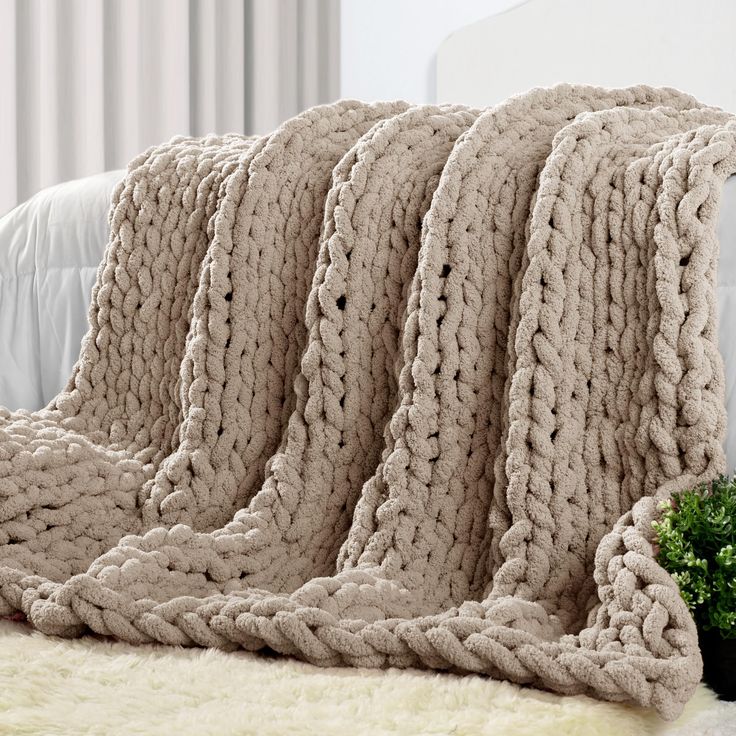 a large chunky knit blanket on a couch next to a small potted plant