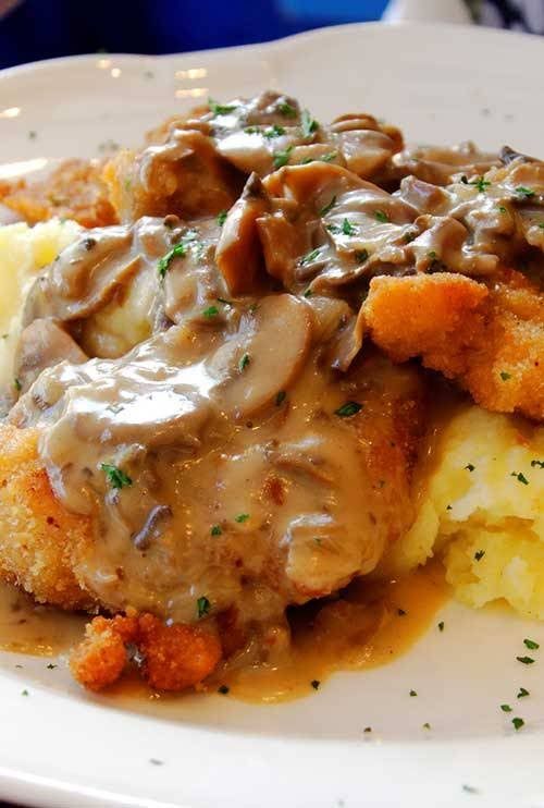 a white plate topped with meat and gravy covered in gravy next to mashed potatoes