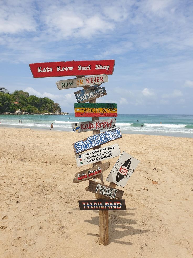 there are many signs on the beach pointing to different shops and locations in each direction