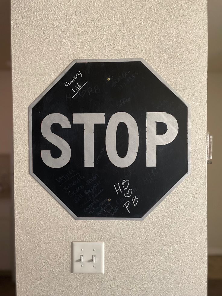 a black and white stop sign with some writing on it's back side, in front of a wall