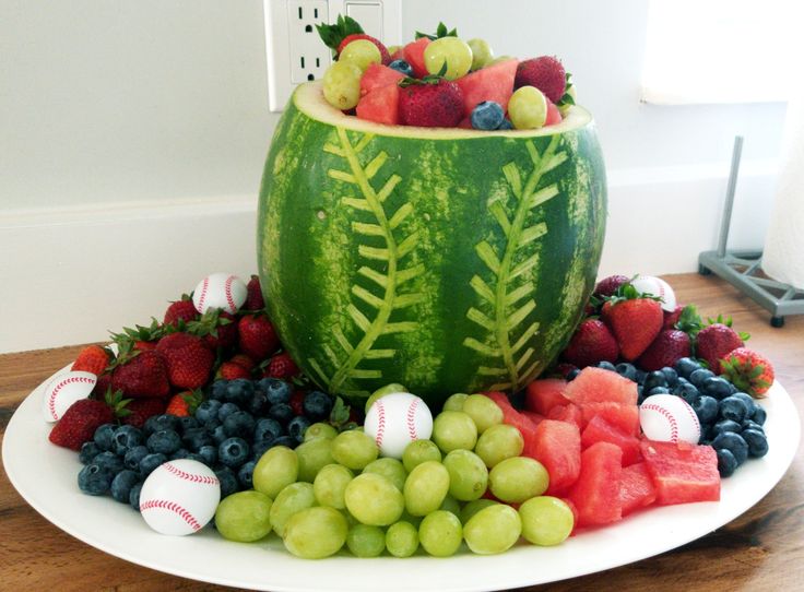 a watermelon with baseballs, grapes and strawberries in it on a plate