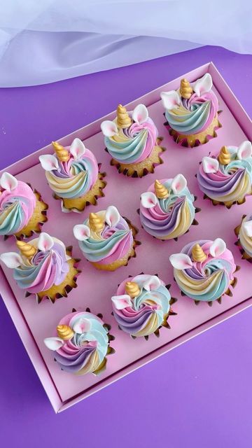 cupcakes decorated with pastel and gold icing in a pink box on a purple surface