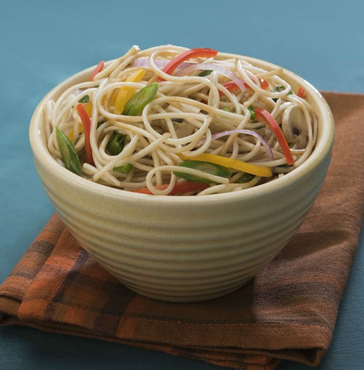 a white bowl filled with noodles and vegetables on top of a brown napkin next to a wooden spoon