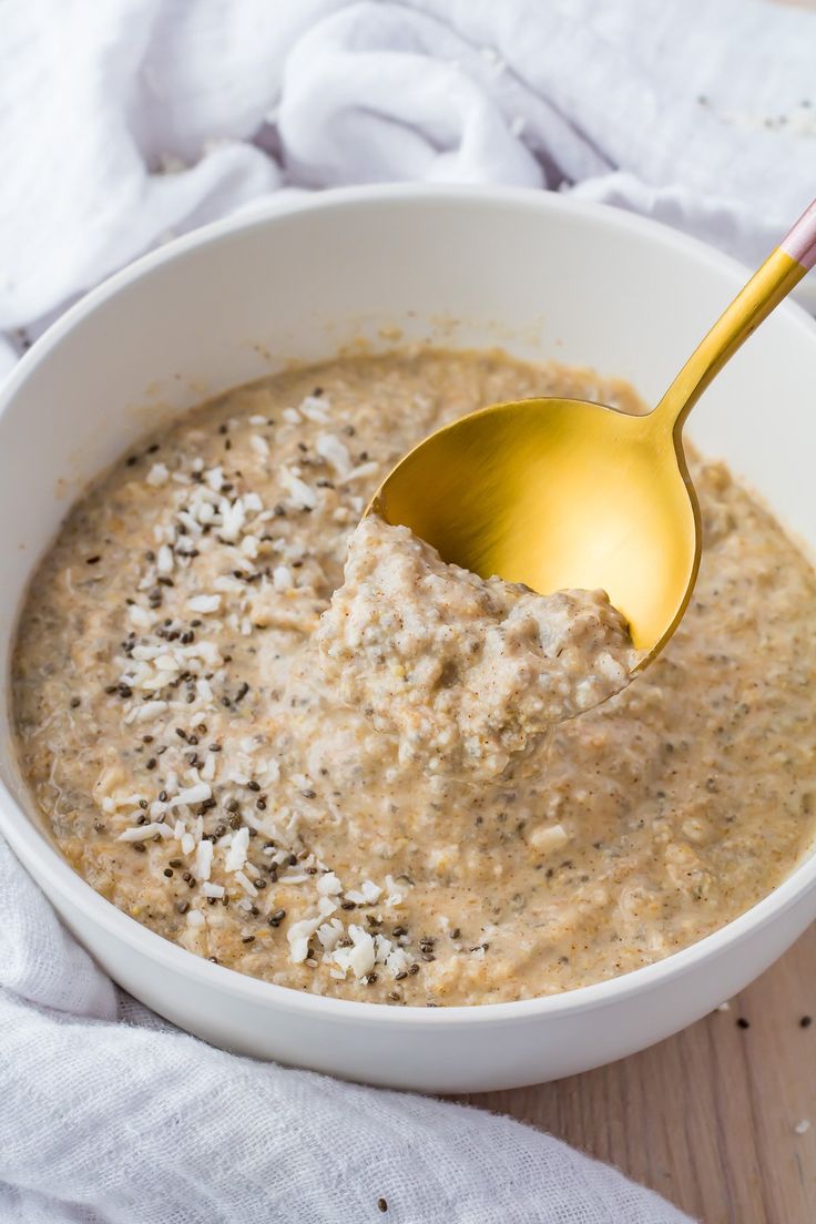 a white bowl filled with oatmeal on top of a wooden table next to a gold spoon