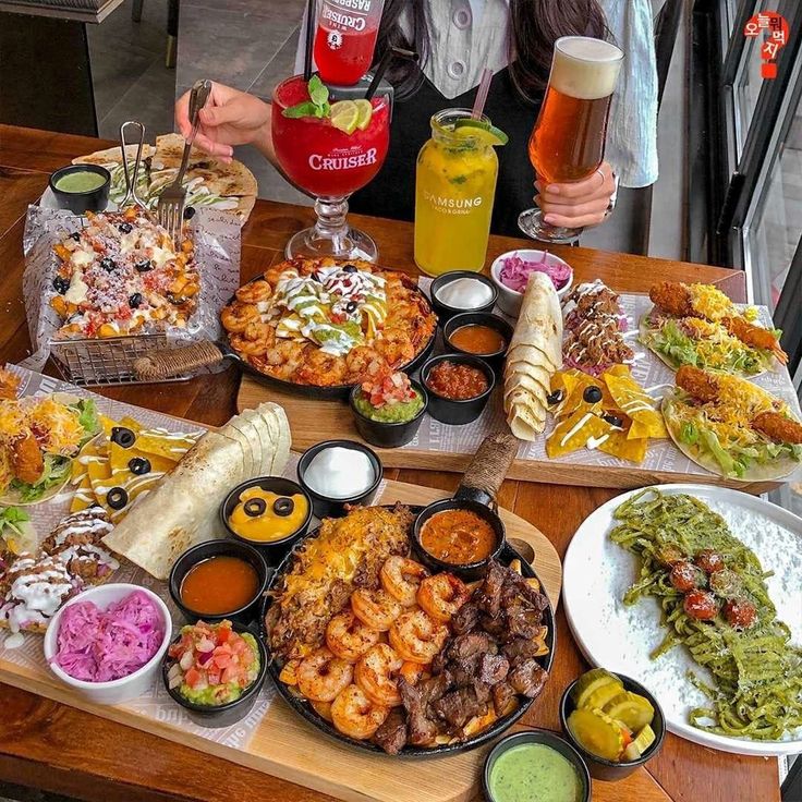 a wooden table topped with lots of different foods and condiments next to drinks