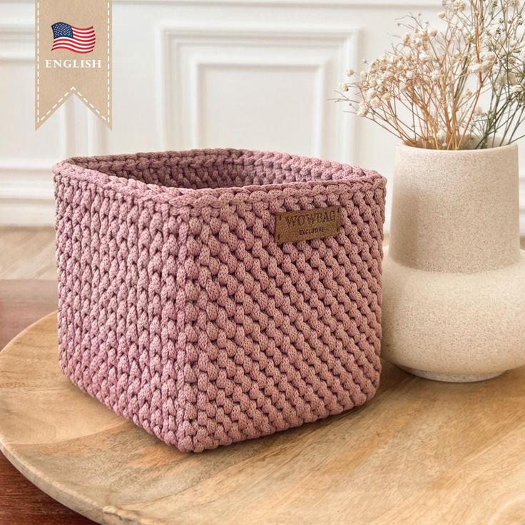 a pink basket sitting on top of a wooden table next to a vase with flowers in it