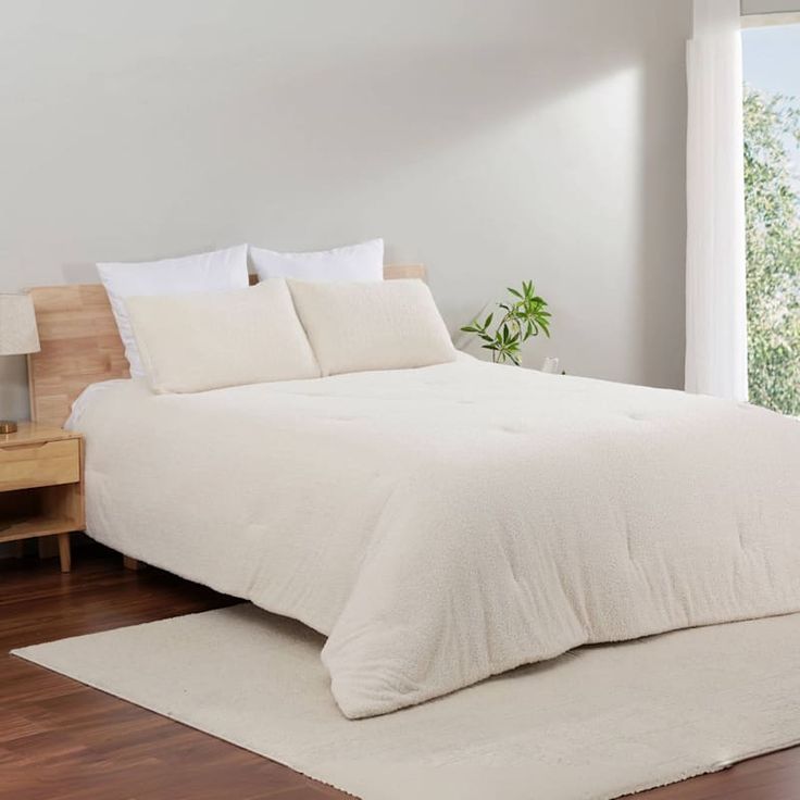 a white bed sitting in a bedroom next to a wooden dresser and window on top of a hard wood floor