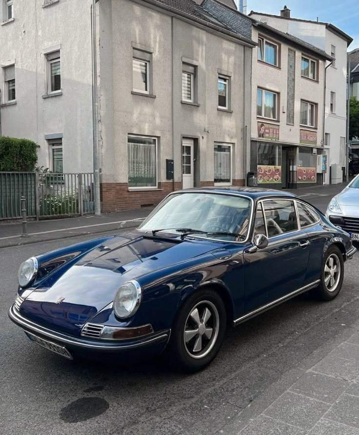 an old blue car parked on the side of the road in front of some buildings