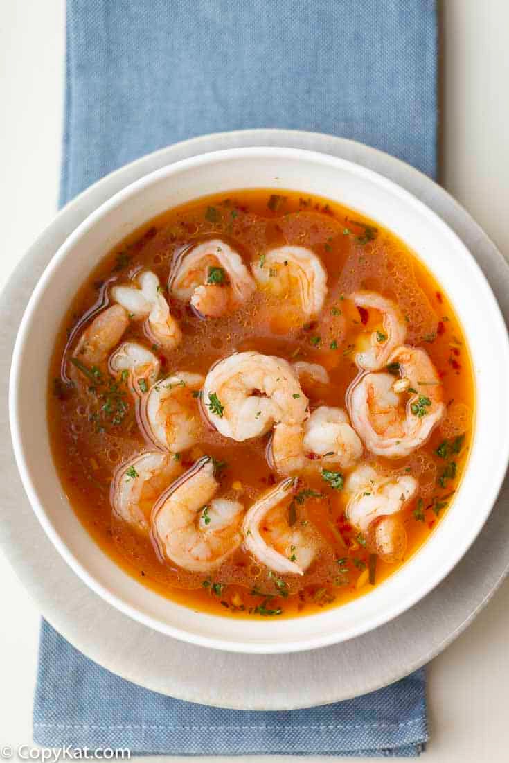 a white bowl filled with shrimp and broth on top of a blue napkin next to a spoon